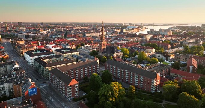 Aerial drone view over Copenhagen city landscape with historic church tower at sunrise.
