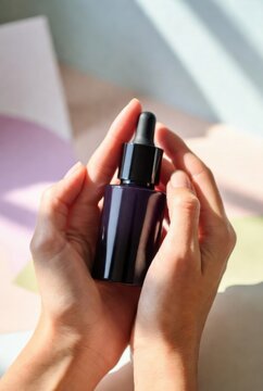 Hands presenting dark cosmetic serum bottle mockup with dropper in soft sunlit setting