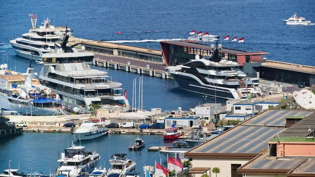 Aerial view of luxury mega yachts docked at the busy harbor in Monaco during a sunny afternoon.