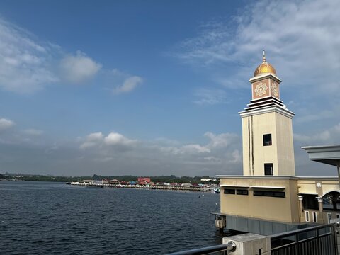 Historic lighthouse on rocky pier overlooking calm coastal cityscape under blue sky