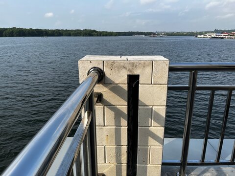 Modern metal railing on stone pier overlooking calm blue lake with distant shoreline view