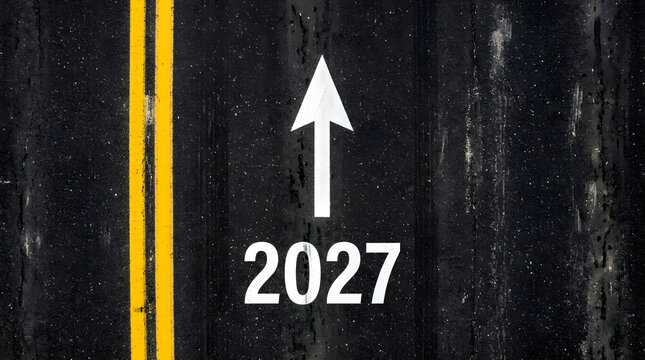 Year 2027 text and forward arrow painted on dark asphalt road surface. Ideal for future planning and business milestone concepts.