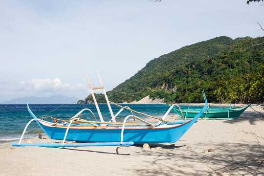 Philippines. Blue outrigger boat on tropical beach with green hillside and turquoise sea