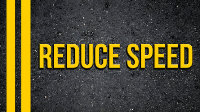 Close-up of bold yellow text reading REDUCE SPEED on dark, rough asphalt surface with a double yellow line on the left side, emphasizing a traffic safety message featuring road sign and pavement