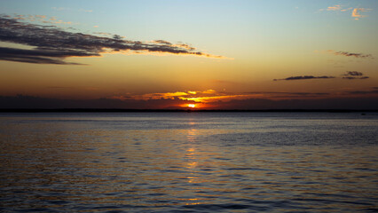Obraz premium A stunning sunset over a calm ocean horizon with a glowing sun dipping below dark golden cloud layers, capturing a peaceful and warm evening atmosphere.