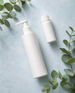 Blank white cosmetic pump and bottle packaging mockup with eucalyptus on blue background