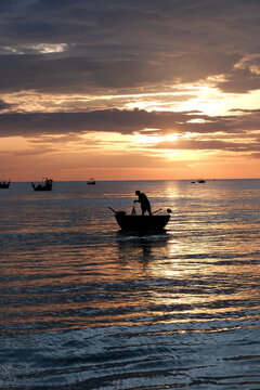Silhouetted view of local fishermen and coracles on the ocean under a glowing morning sky in a Da Nang fishing community
