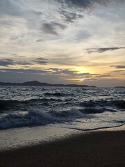 Obraz premium Golden sunset over dark sea waves washing onto sandy beach shore.