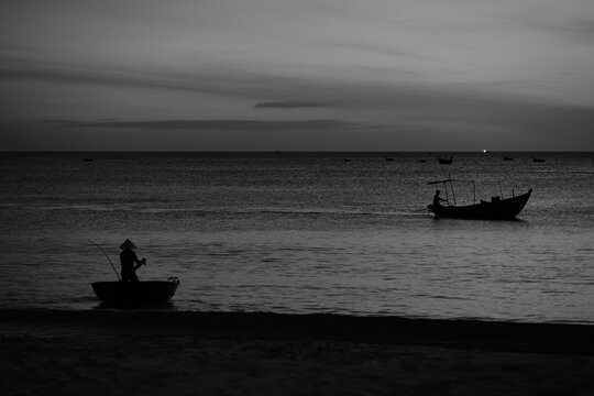 Fine art black and white photograph of the sea at early twilight with a coracle boat setting out and a passing fishing boat