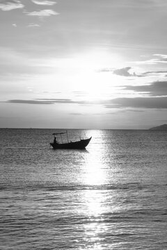  Black and white photograph of a fishing boat passing through a shimmering beam of sunrise light on the sea in Da Nang