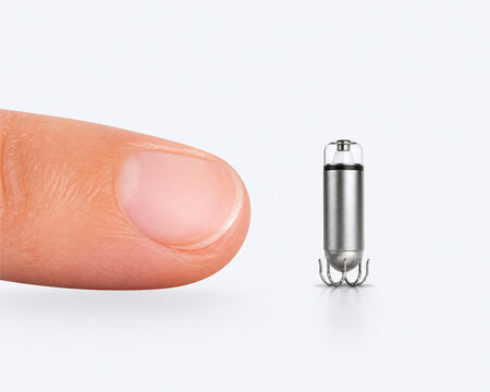 Tiny leadless pacemaker beside fingertip for size comparison