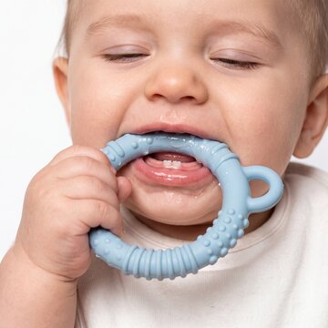Baby chewing on a blue teether with erupting bottom teeth