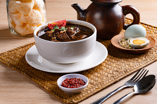 Traditional rawon beef soup setup featuring clay teapot and condiments