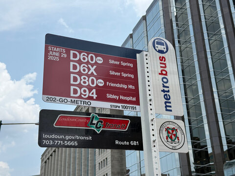 Metrobus and Loudoun County Transit bus stop sign listing routes D60, D6X, D80, D94 and 681 beside a modern office building - Washington, District of Columbia, USA - July 27, 2026