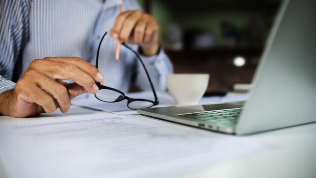 close-up shot, businessman holding eyeglasses work on desk with laptop and document meeting online via wireless technology