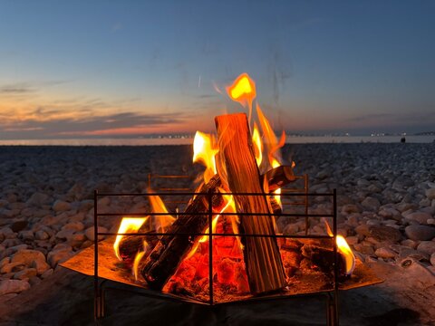 Bonfire burning in a portable fire pit on a pebble beach at dusk by the sea