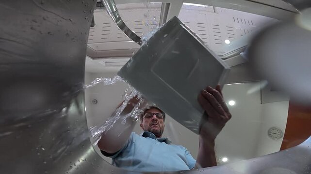 Low-angle view from inside a kitchen sink as a man hurriedly washes dishes in a messy, careless manner, splashing water and leaving dishes poorly cleaned.