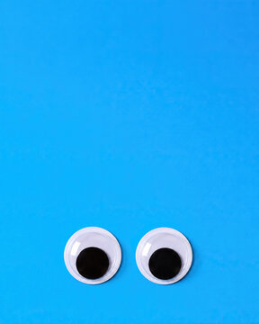 Two Googly Eyes Placed On A Bright Blue Solid Background