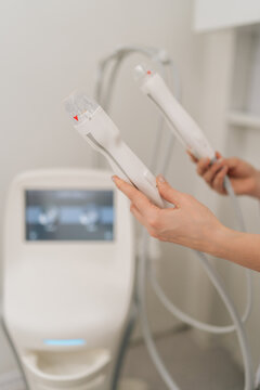 Closeup of unrecognizable beautician holding handles of fractional radiofrequency device, preparing for a non surgical facial lifting and skin tightening treatment in a modern beauty clinic.