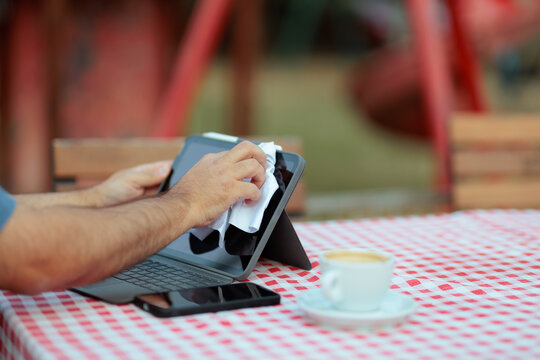 Close Up Of Man Wiping Digital Tablet Screen With Microfiber Cloth. Person cleans the display of a tablet using a white napkin outdoors