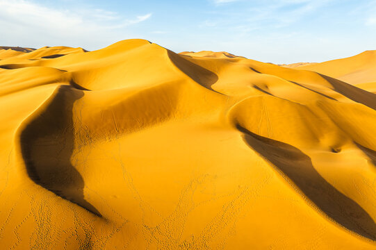 Golden sand dunes with curved ridges under clear sky in Kumtag Desert, Xinjiang, China.