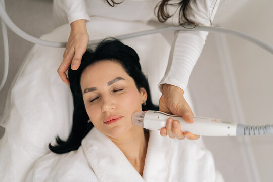 Closeup of professional cosmetologist performing microneedle rf lifting procedure on middle-aged female client face for skin rejuvenation, antiaging effects, facial contouring in modern clinic.