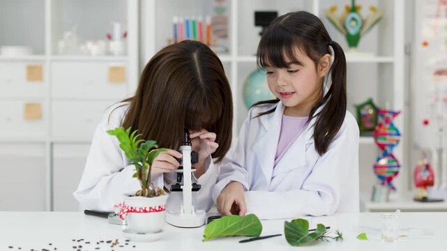 Asian Elementary Students in Lab Coats Using Microscope for Biology Experiment