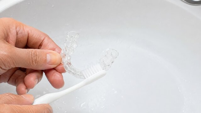 Cleaning clear orthodontic retainer with toothbrush over sink
