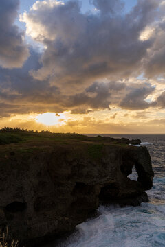 夕暮れ時の万座毛と断崖絶壁に差し込む夕日・沖縄県恩納村（縦型）the Manzamo cliff and ocean in Onna Village, Okinawa
