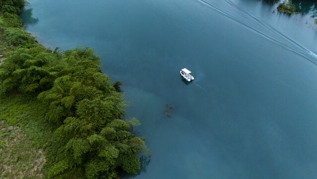 Aerial view of a small boat cruising on the calm blue waters of a river surrounded by dense green vegetation in Urhuoka, Delta, Nigeria.
