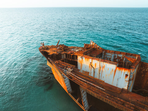 Aerial view of Gulf Dove shipwreck showing rusted metal hull and deck structures surrounded by clear turquoise sea water with people standing on the bow in Hulaf, Yemen.