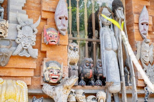 BALI, INDONESIA &ndash; OCTOBER 20, 2024: Traditional Balinese wooden masks and tribal sculptures displayed on a red brick wall.