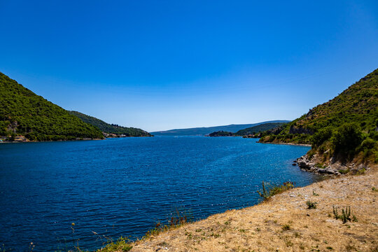 A wide strait of blue water framed by green hills and rocky shore under a clear sky.