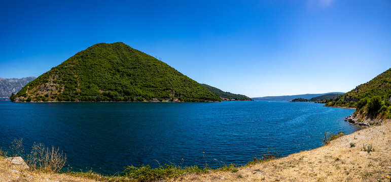 A wide strait of blue water framed by green hills and rocky shore under a clear sky.