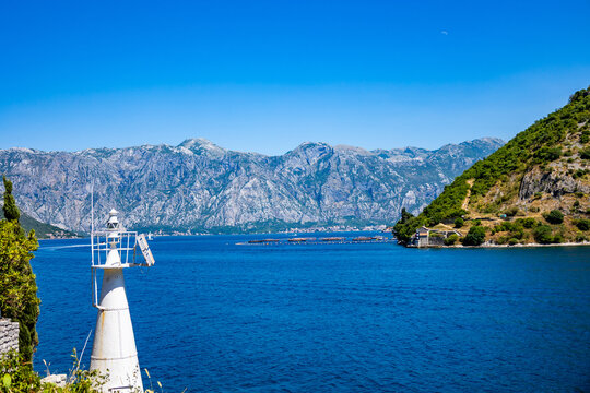 Panoramic view of Kotor Bay with calm blue water, rocky mountains, and clear blue sky in Montenegro.