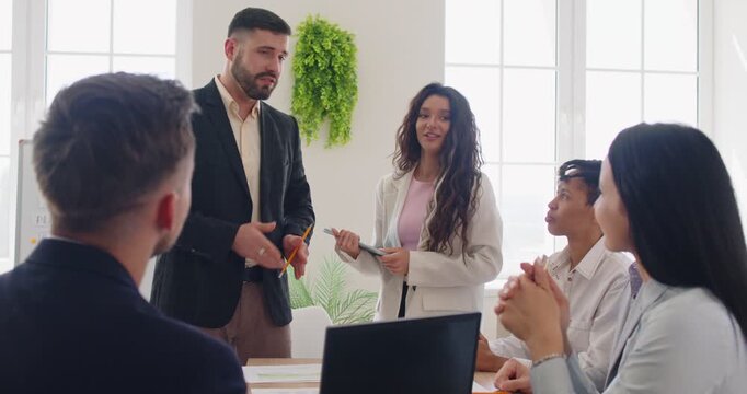 Group of diverse businesspeople listening to man presenting and gesturing, attentively listening, watching, discussing ideas, collaborating on new project, conducting business meeting, mentoring