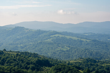 Naklejka premium A panoramic view of a vast mountainous landscape from high elevation, dominated by dense forests and open fields in the foreground