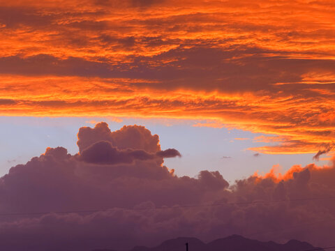 Dramatic fiery orange sunset with towering storm clouds dark vertical cloud formations glowing red sky atmospheric weather phenomenon intense nature cloudscape background