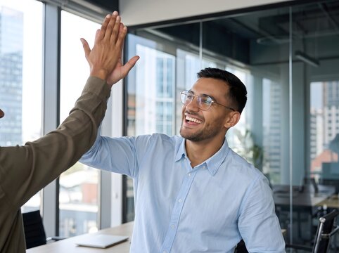 Two happy business people giving a high-five in a modern office, celebrating success and teamwork.