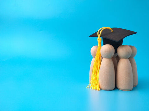 A group of wooden peg figures wears a black graduation cap with a yellow tassel on a blue background