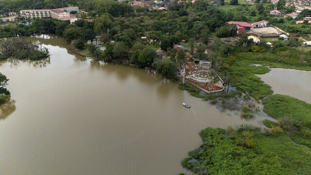 Aerial view of Nike Lake surrounded by lush greenery, trees, and resort buildings, with a small boat navigating the calm brown waters in Enugu East, Enugu, Nigeria.