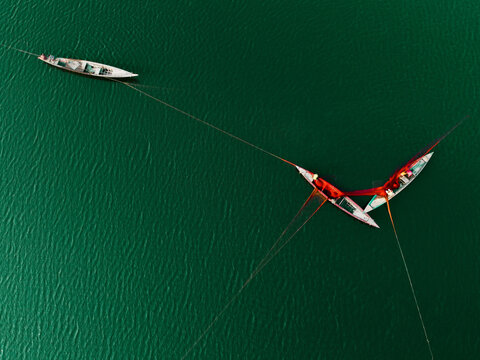 Aerial view of traditional fishing boats on a river with fishermen using large nets to catch fish in the green water of Bogura, Rajshahi Division, Bangladesh.