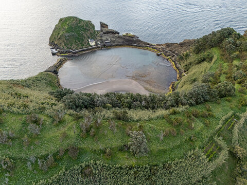 Aerial view of the volcanic crater lake at Ilheu de Vila Franca do Campo surrounded by lush green vegetation and rocky cliffs in the Atlantic Ocean, Sao Pedro, Acores, Portugal.
