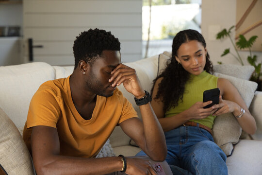 African American couple sitting on sofa, man holding phone, woman wearing lime top scrolling phones