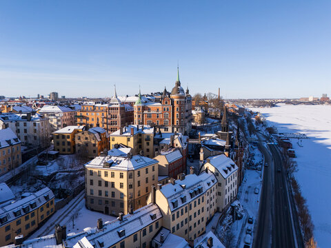 Aerial view of historic buildings with snow-covered rooftops, a frozen waterway, and a road along the waterfront in Stockholm, Stockholm County, Sweden.