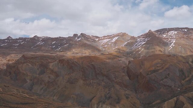 Wide angle shot of dry Himalayan mountain range with patches of snow on mountain peaks with clouds above them during the summer season as seen from Tanglang La on Leh Manali highway in Ladakh, India.