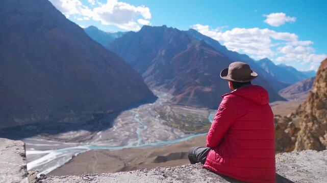 Indian male tourist wearing hat and jacket looking the dry Himalayan mountain peaks along with confluence of Pin and Spiti river at Dhankar Monastery in Spiti Valley, Himachal Pradesh, India.