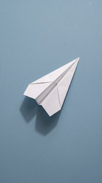 White paper airplane casting a soft shadow on a minimalist blue background, symbolizing launch, startup, and creative ideas