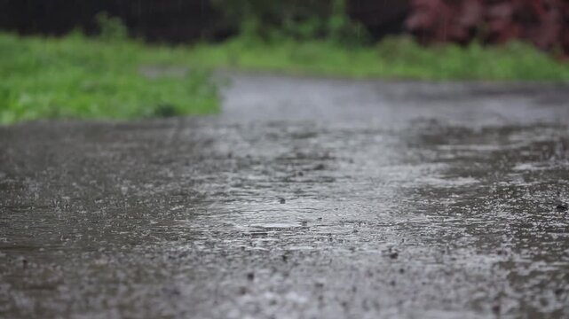 Rain Shower Splashing into Water Puddle on Rural Road. Mood-setting footage capturing continuous raindrops falling onto a wet tar road during a stormy overcast day in the countryside.