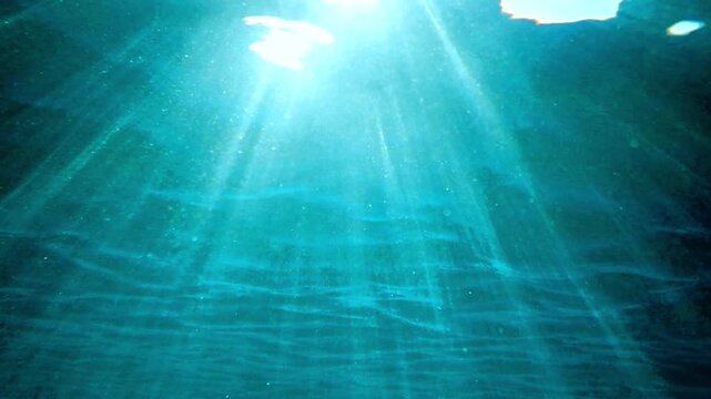 Dark blue ocean surface seen from underwater. Sunlight rays under water. Underwater blue background in sea bottom. Sunbeam and ripples. wave lights. Slow motion. Mediterranean sea. Real video water.